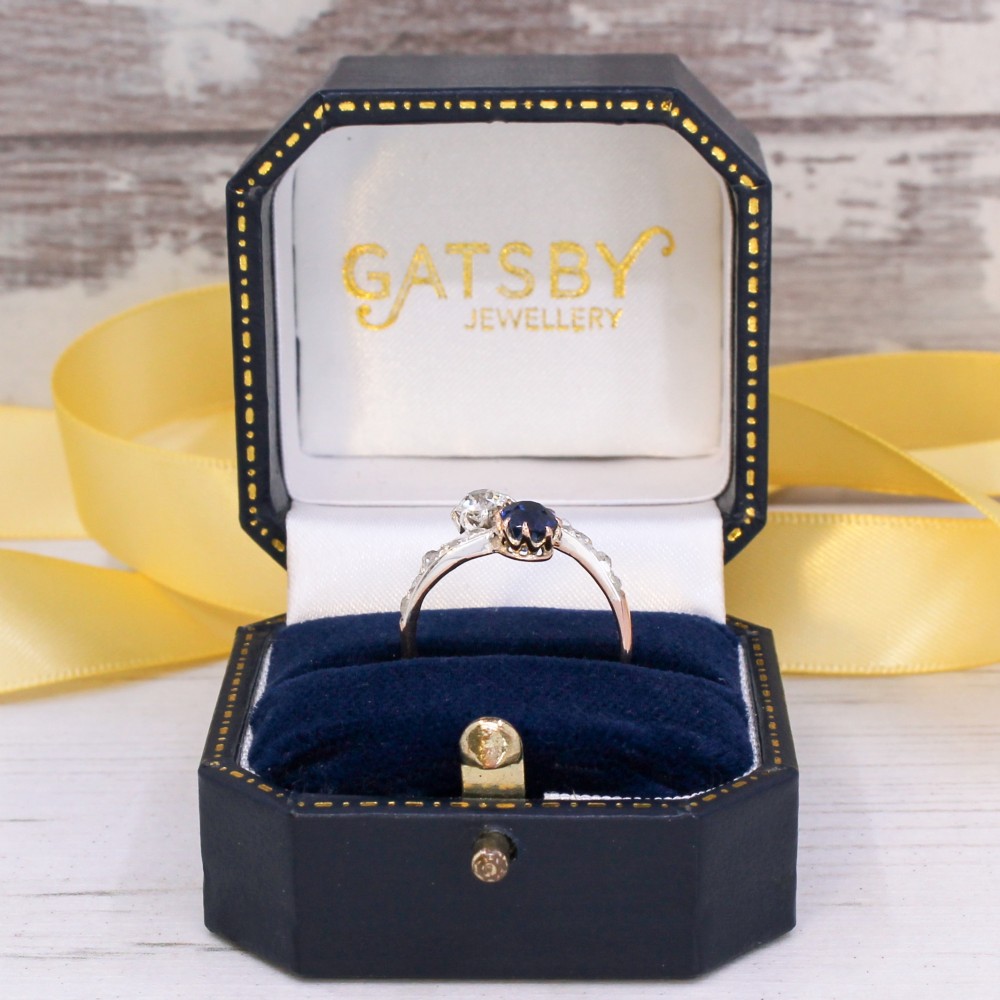 An antique Edwardian gold and platinum crossover ring set with a round blue sapphire and a diamond in a Moi et Toi design. View IX