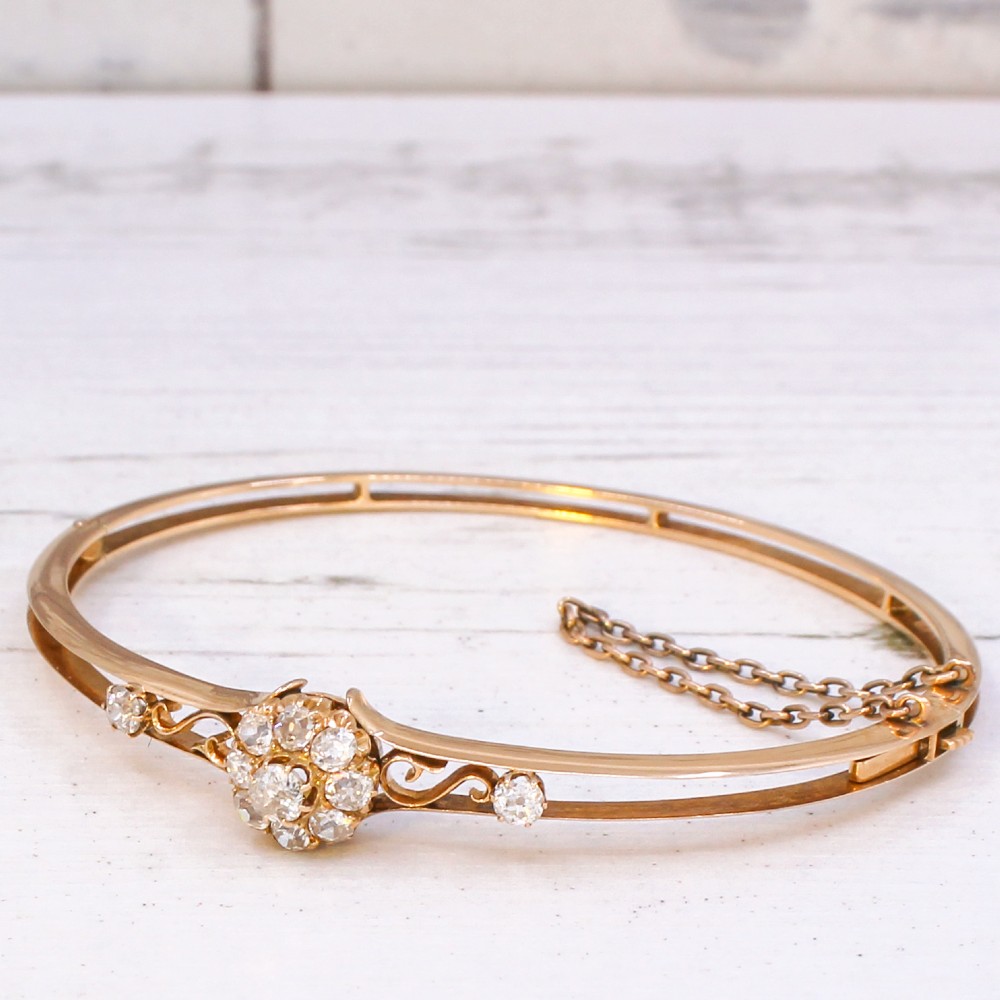 A late Victorian yellow gold hinged bangle featuring a central old-cut diamond cluster flanked by scrollwork and accent diamonds.