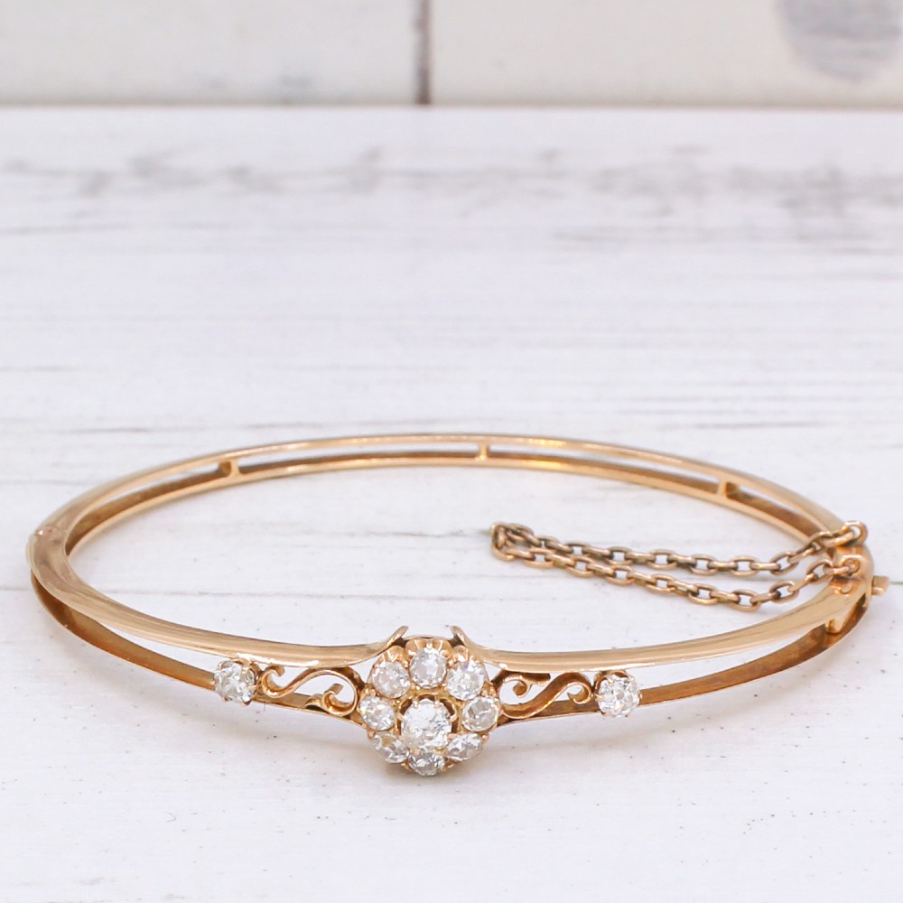 A late Victorian yellow gold hinged bangle featuring a central old-cut diamond cluster flanked by scrollwork and accent diamonds. View IV