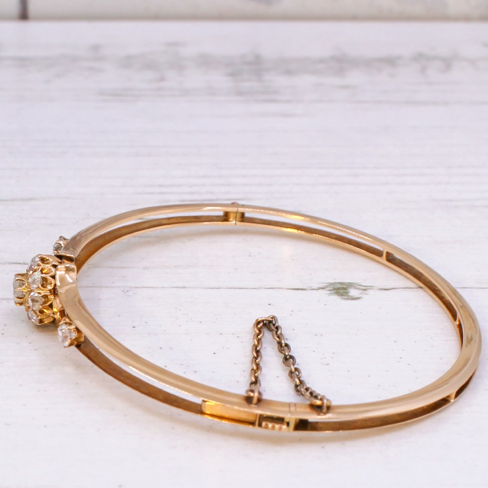A late Victorian yellow gold hinged bangle featuring a central old-cut diamond cluster flanked by scrollwork and accent diamonds. View V