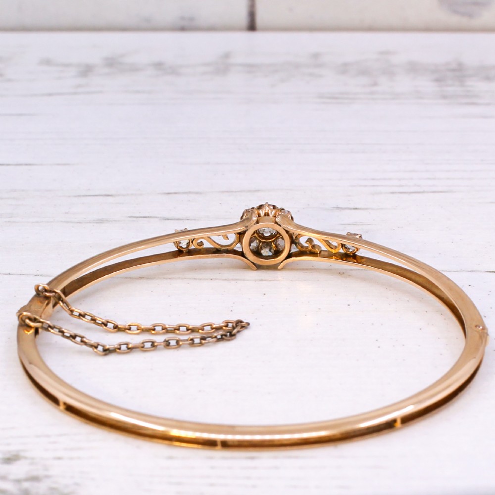 A late Victorian yellow gold hinged bangle featuring a central old-cut diamond cluster flanked by scrollwork and accent diamonds. View VI