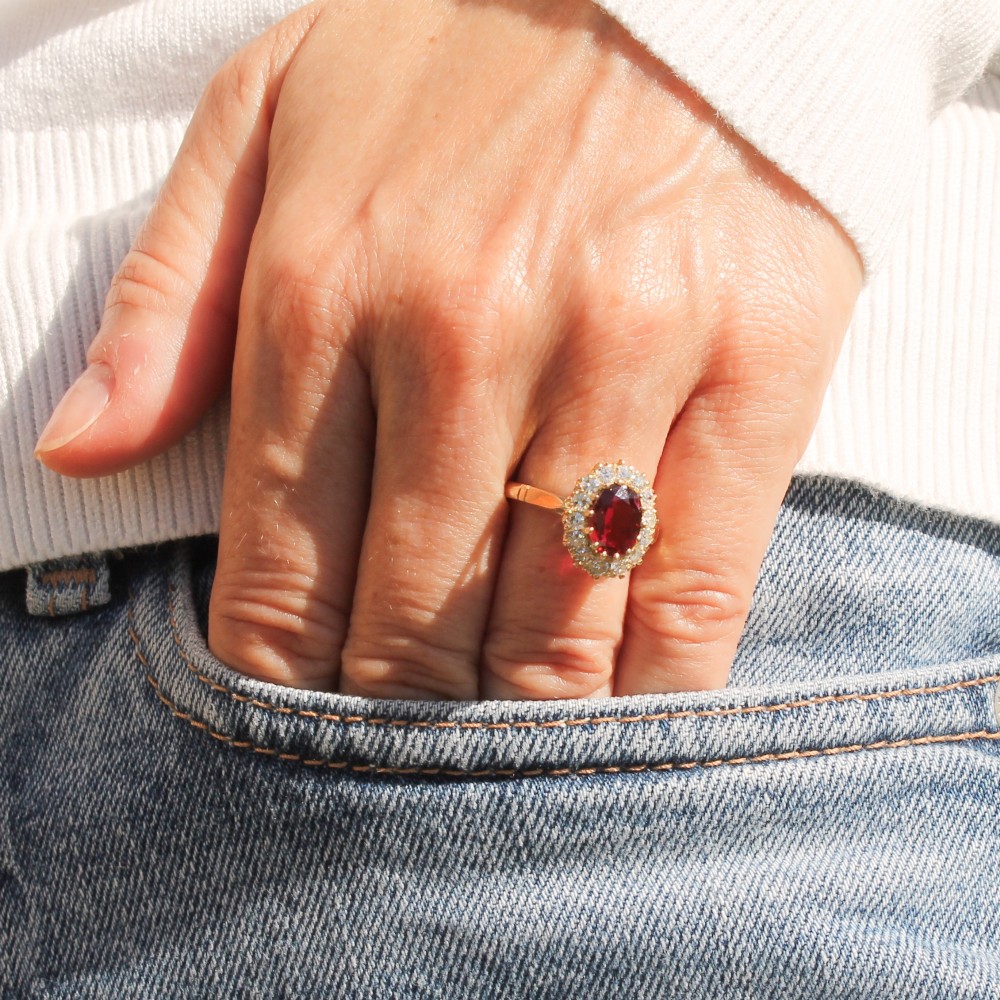 A vintage yellow gold ring featuring a central oval-cut red ruby framed by a halo of brilliant round diamonds. View II