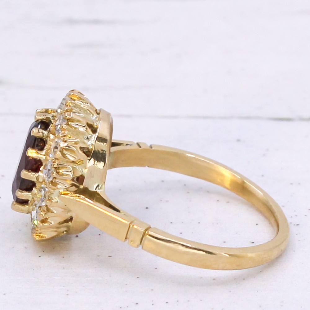 A vintage yellow gold ring featuring a central oval-cut red ruby framed by a halo of brilliant round diamonds. View IV