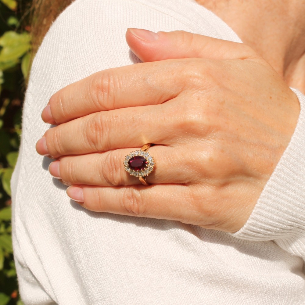 A vintage yellow gold ring featuring a central oval-cut red ruby framed by a halo of brilliant round diamonds. View VII