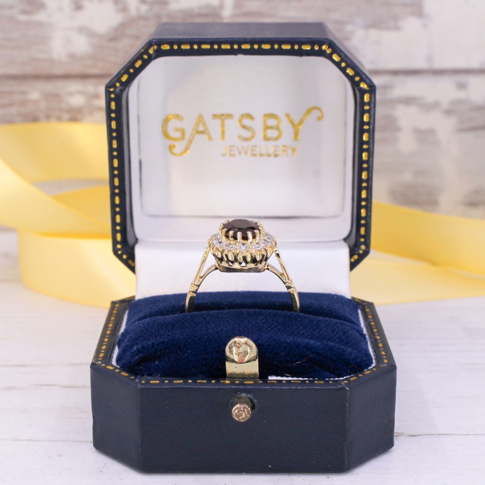 A vintage yellow gold ring featuring a central oval-cut red ruby framed by a halo of brilliant round diamonds. View IX