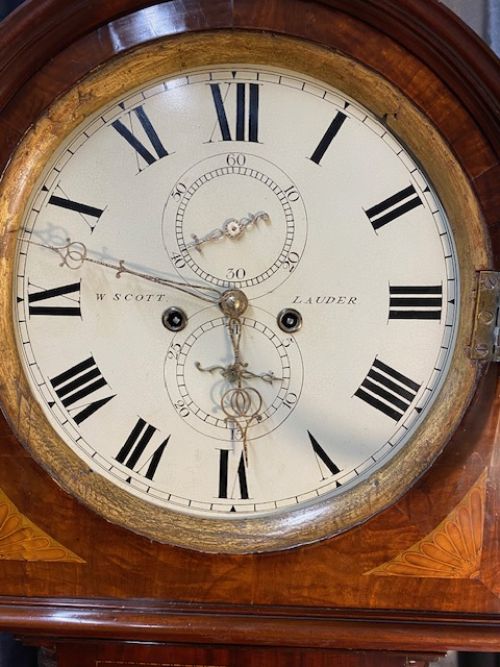 fig 1. A tall mahogany longcase clock featuring elaborate decorative marquetry inlays on the central door and a circular Roman numeral dial under an arched hood.