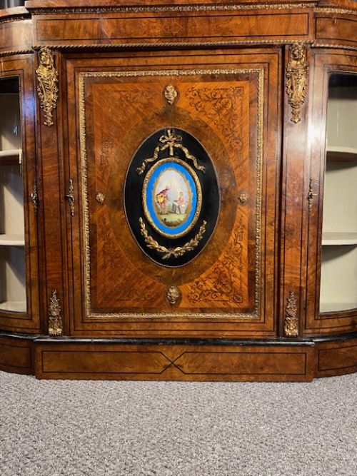 fig 1. A Victorian burr walnut credenza with a central marquetry door featuring an oval porcelain plaque flanked by two curved glazed doors.