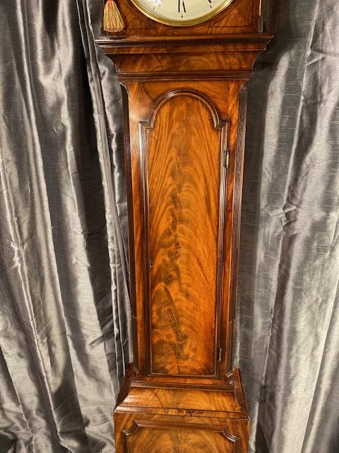 fig 3. A tall antique flame mahogany longcase clock featuring an arched dial with Roman numerals signed James McCabe London and topped with a brass finial.