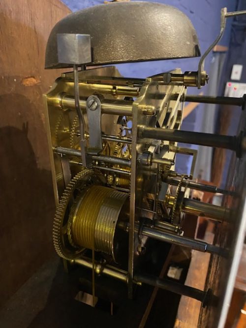 fig 1. A tall antique flame mahogany longcase clock featuring an arched dial with Roman numerals signed James McCabe London and topped with a brass finial.