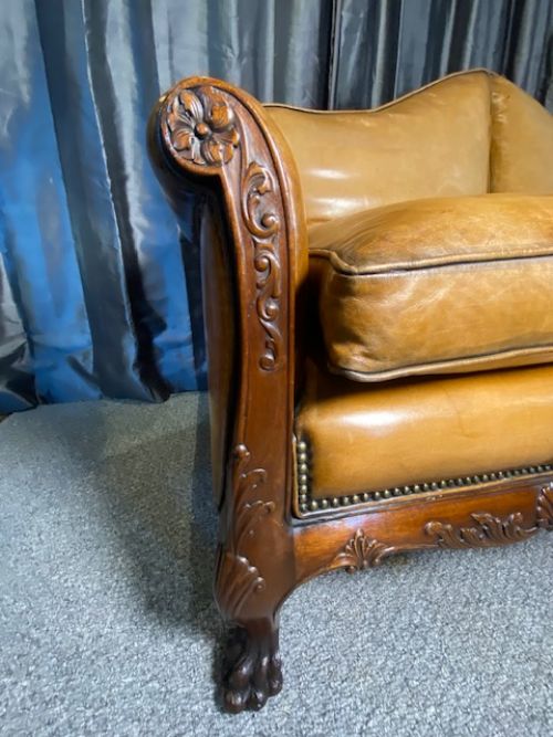 fig 1. A two-seater settee upholstered in tan leather featuring shaped back cushions, studding detail, a carved dark wood apron, and ball-and-claw feet.