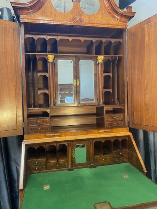 fig 2. An antique walnut bureau bookcase featuring a broken arch pediment, double mirrored cabinet doors, a slant-front writing slope, and several drawers with brass handles.