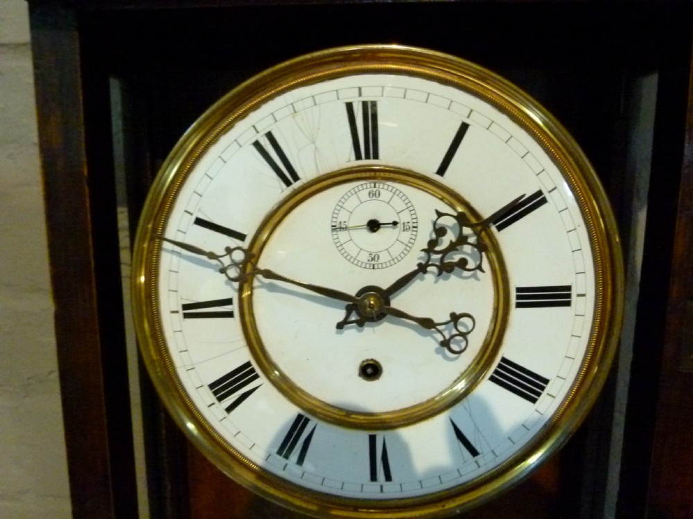 A mahogany wall-mounted regulator clock with a scroll pediment, white dial with Roman numerals, and visible brass weight and pendulum within a glazed door. View II