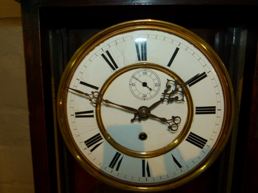 A mahogany wall-mounted regulator clock with a scroll pediment, white dial with Roman numerals, and visible brass weight and pendulum within a glazed door. View III