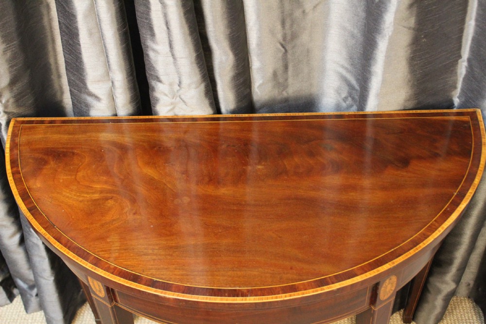 A semi-circular antique mahogany demilune card table featuring satinwood stringing inlays and slender tapered legs. View II