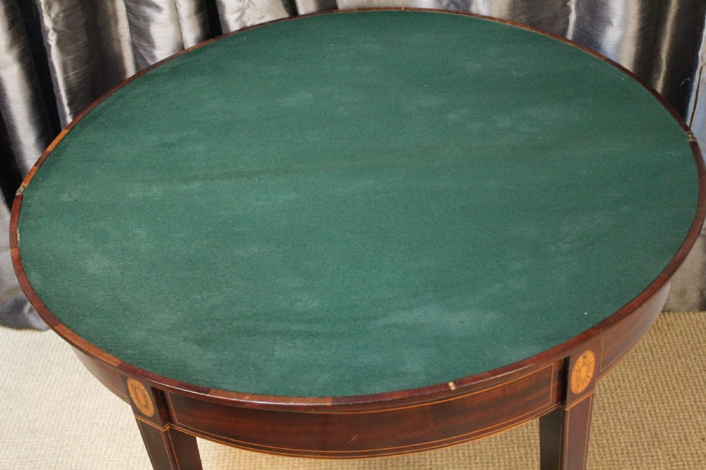 A semi-circular antique mahogany demilune card table featuring satinwood stringing inlays and slender tapered legs. View IV