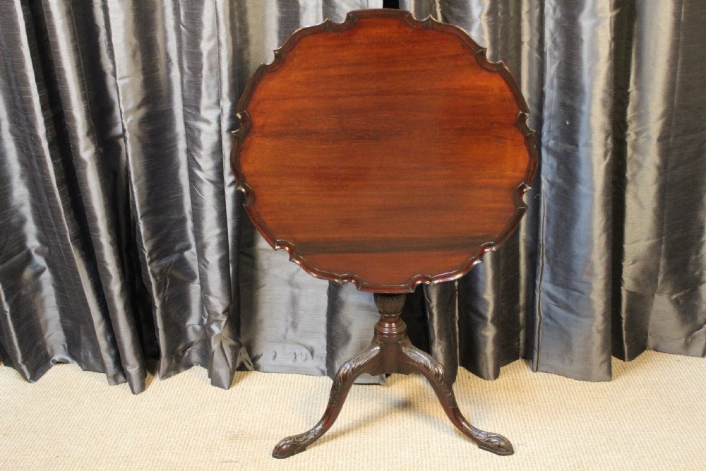 A mahogany tilt-top occasional table featuring a scalloped piecrust rim, turned column, and carved tripod legs.