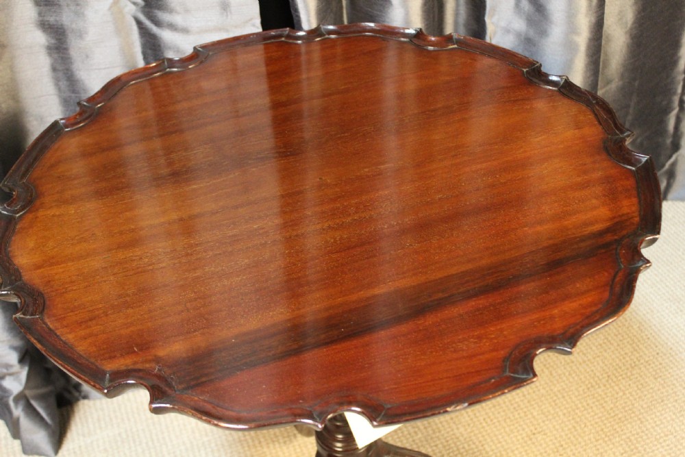 A mahogany tilt-top occasional table featuring a scalloped piecrust rim, turned column, and carved tripod legs. View II