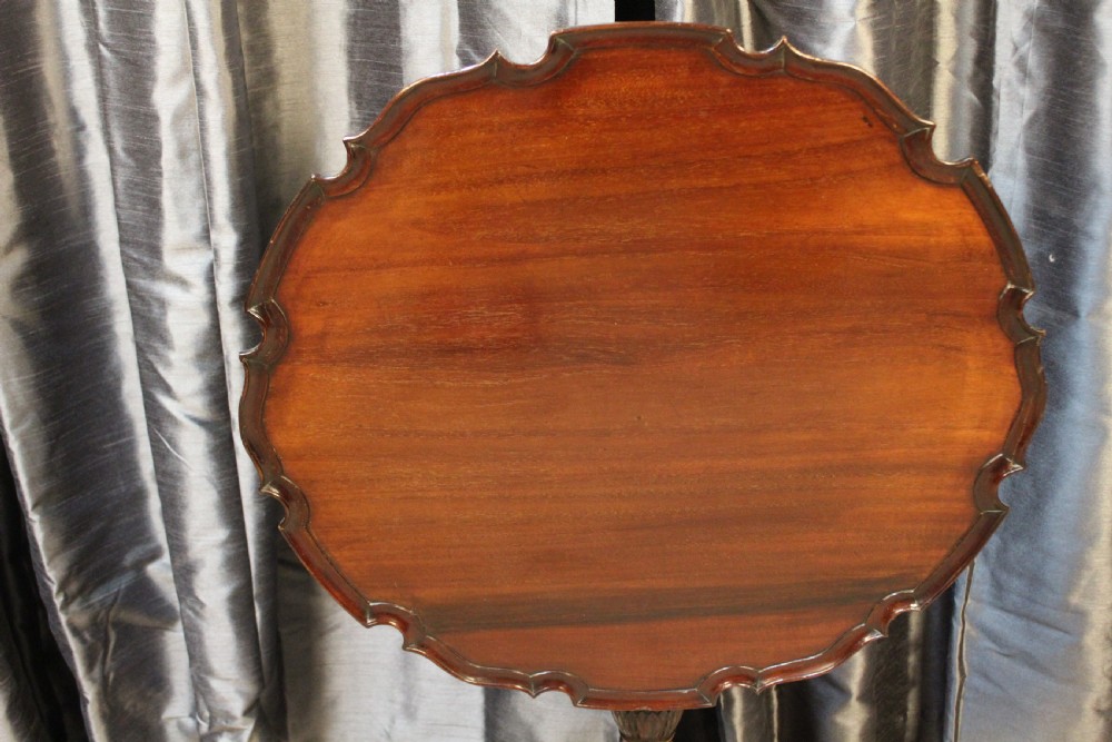 A mahogany tilt-top occasional table featuring a scalloped piecrust rim, turned column, and carved tripod legs. View IV