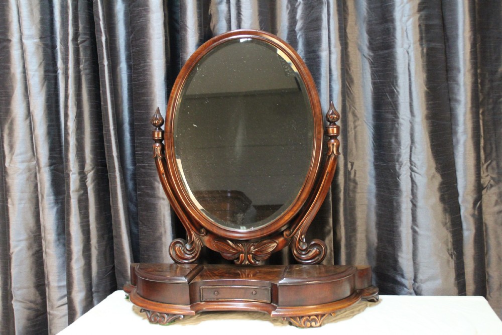 A Victorian mahogany dressing table mirror with an oval glass frame supported by carved scroll pillars on a plinth base.