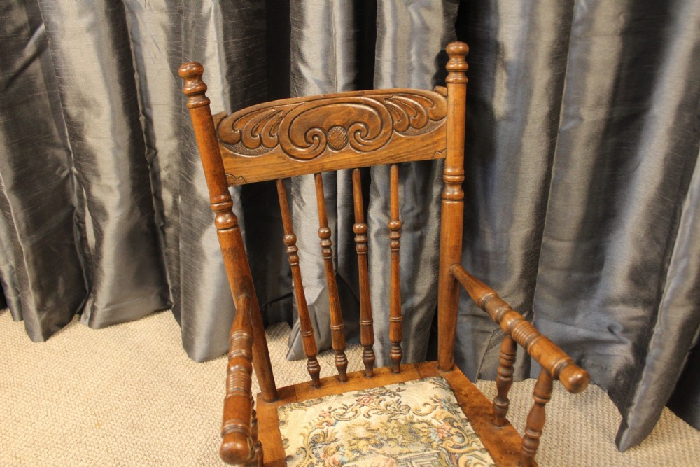 A small antique carved oak childs armchair featuring turned spindles, armrests, and a tapestry upholstered seat cushion. View II