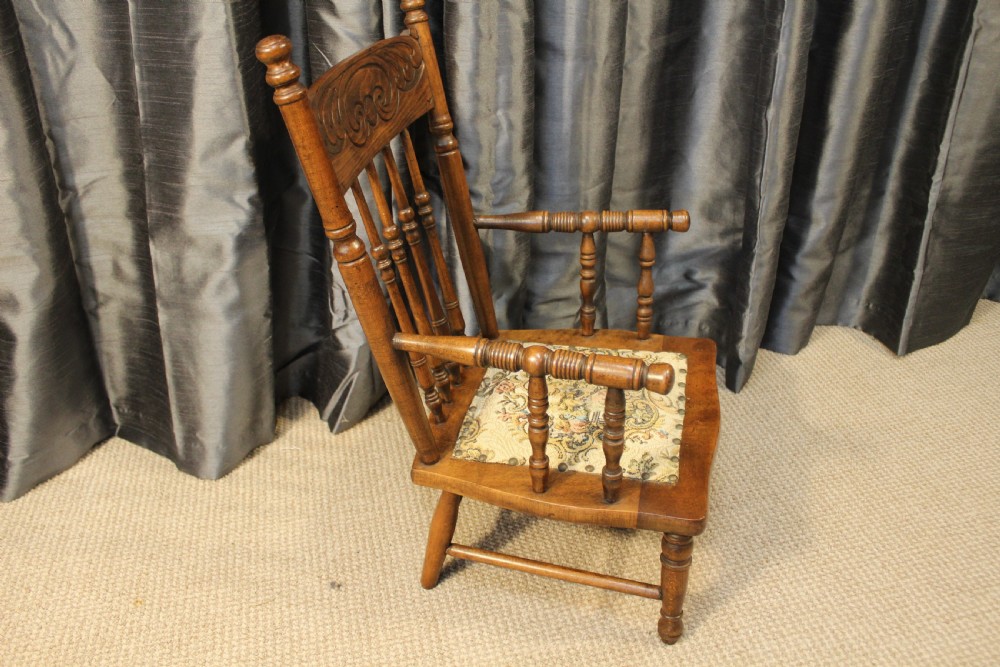 A small antique carved oak childs armchair featuring turned spindles, armrests, and a tapestry upholstered seat cushion. View III