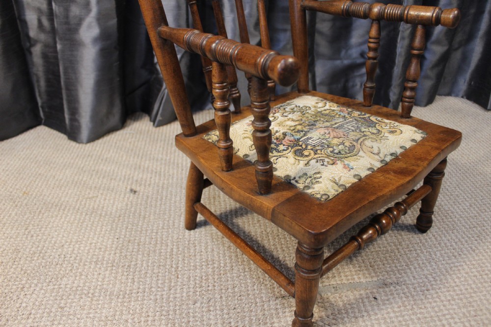A small antique carved oak childs armchair featuring turned spindles, armrests, and a tapestry upholstered seat cushion. View IV