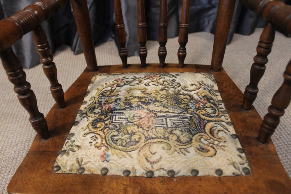 A small antique carved oak childs armchair featuring turned spindles, armrests, and a tapestry upholstered seat cushion. View V