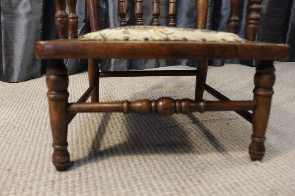 A small antique carved oak childs armchair featuring turned spindles, armrests, and a tapestry upholstered seat cushion. View VI
