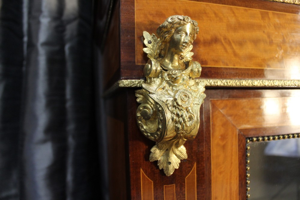 An antique warm brown timber cabinet featuring a glazed front door, ornamental gilt metal mounts, and porcelain floral plaques. View IV