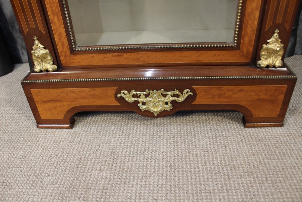 An antique warm brown timber cabinet featuring a glazed front door, ornamental gilt metal mounts, and porcelain floral plaques. View VII