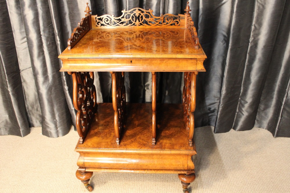 A Victorian burr walnut music Canterbury featuring a carved fretwork gallery, vertical scroll partitions, a lower drawer, and turned legs with castors.