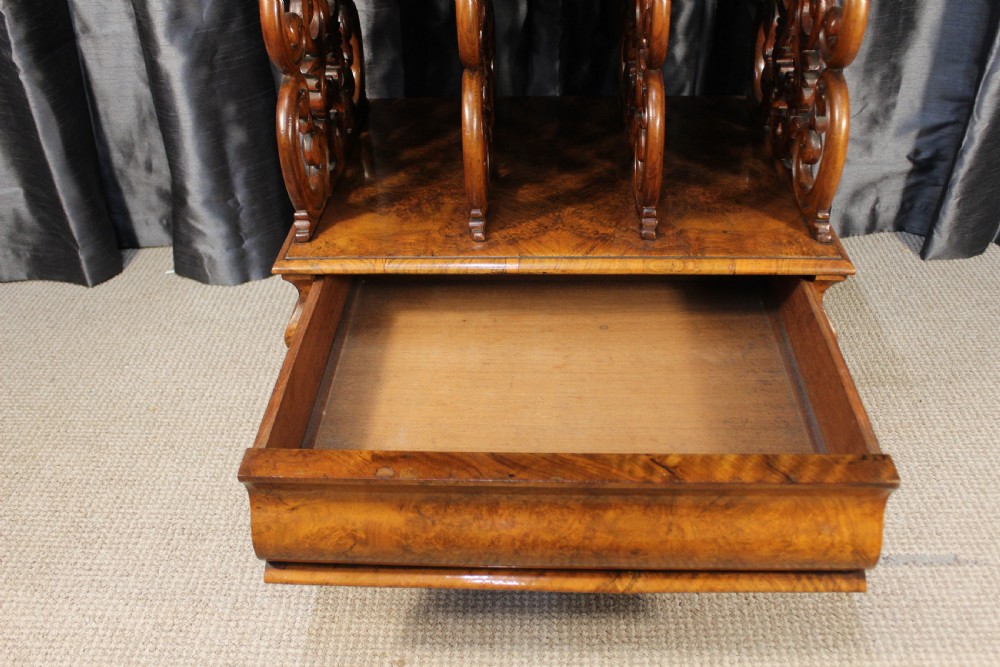 A Victorian burr walnut music Canterbury featuring a carved fretwork gallery, vertical scroll partitions, a lower drawer, and turned legs with castors. View IV