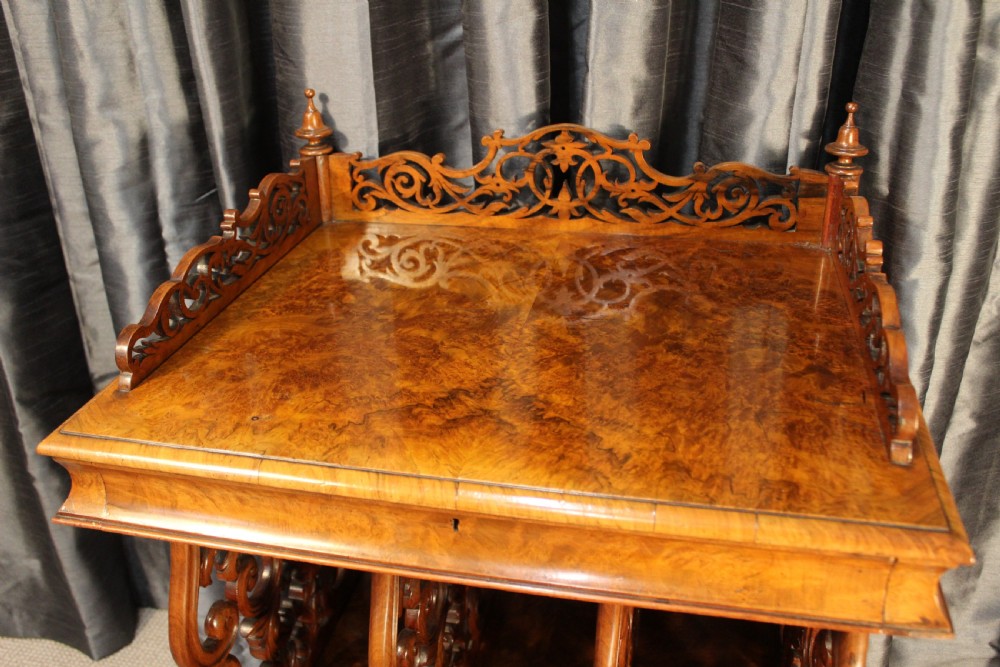 A Victorian burr walnut music Canterbury featuring a carved fretwork gallery, vertical scroll partitions, a lower drawer, and turned legs with castors. View V
