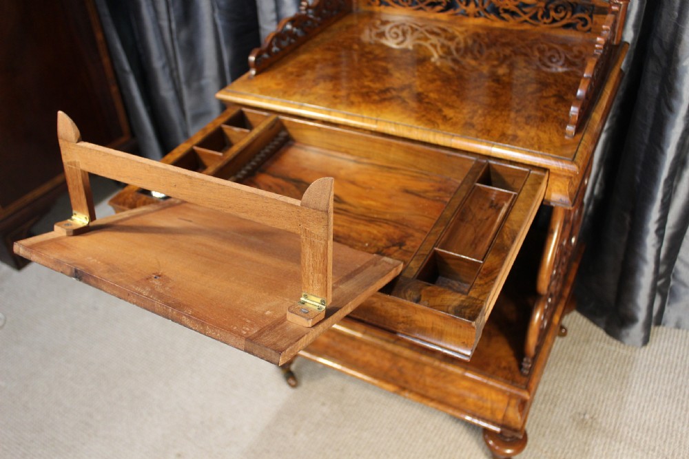 A Victorian burr walnut music Canterbury featuring a carved fretwork gallery, vertical scroll partitions, a lower drawer, and turned legs with castors. View VI