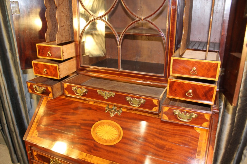 An antique mahogany bureau bookcase featuring an arched glazed upper door, oval marquetry inlays, a slant-front writing desk, four drawers with brass handles, and bracket feet. View IV