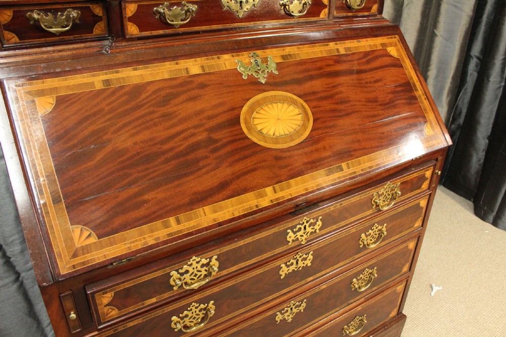 An antique mahogany bureau bookcase featuring an arched glazed upper door, oval marquetry inlays, a slant-front writing desk, four drawers with brass handles, and bracket feet. View V