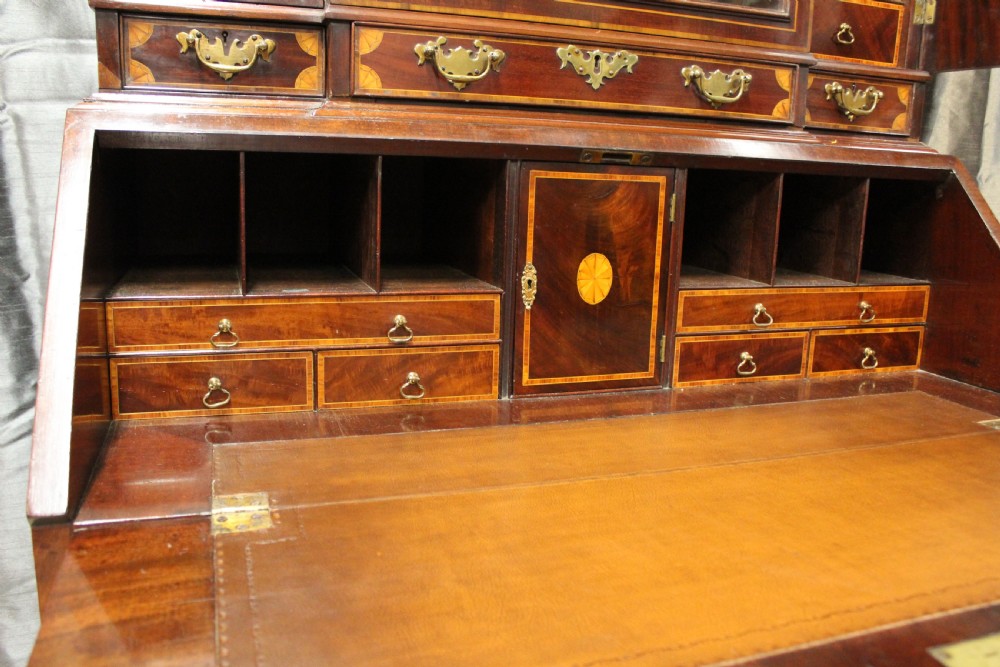 An antique mahogany bureau bookcase featuring an arched glazed upper door, oval marquetry inlays, a slant-front writing desk, four drawers with brass handles, and bracket feet. View VII