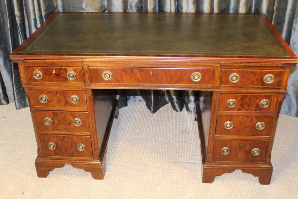 An antique mahogany pedestal desk with nine drawers, circular brass ring handles, flame mahogany drawer fronts, and bracket feet. View II