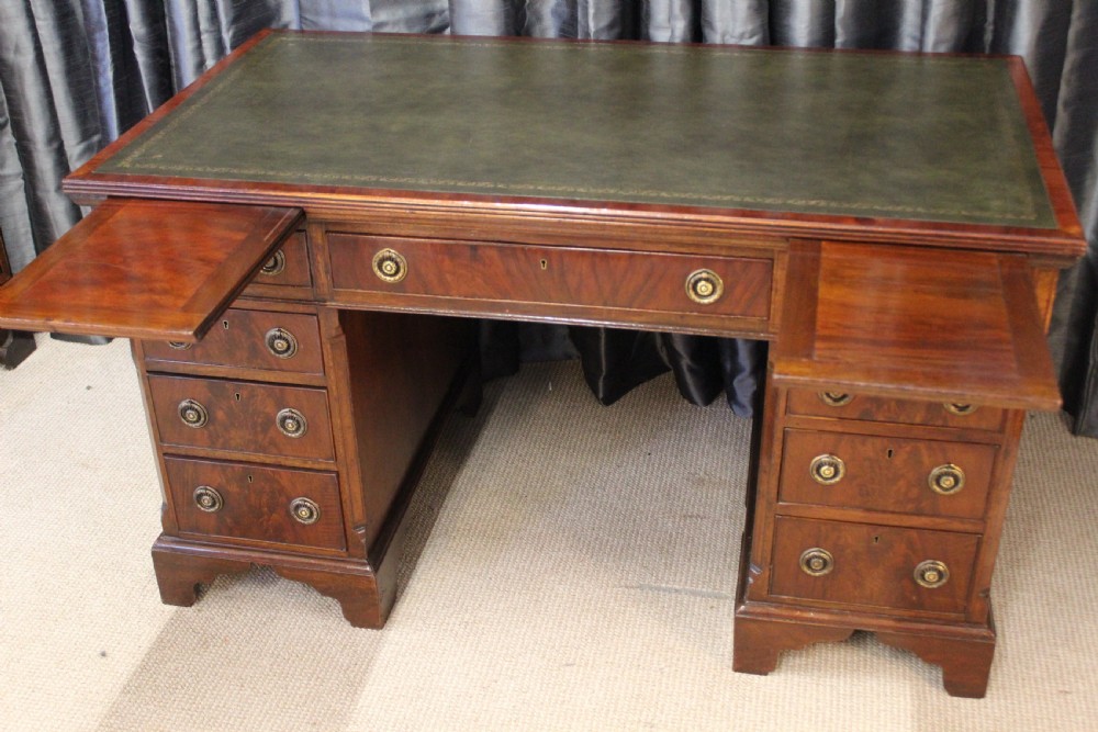 An antique mahogany pedestal desk with nine drawers, circular brass ring handles, flame mahogany drawer fronts, and bracket feet. View III
