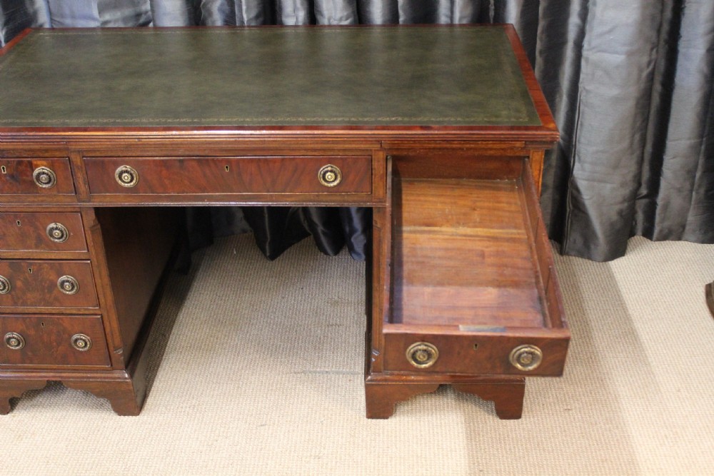 An antique mahogany pedestal desk with nine drawers, circular brass ring handles, flame mahogany drawer fronts, and bracket feet. View IV