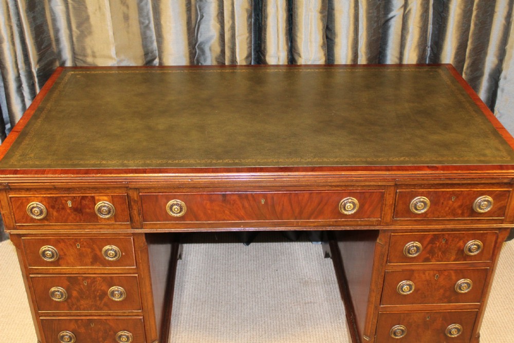 An antique mahogany pedestal desk with nine drawers, circular brass ring handles, flame mahogany drawer fronts, and bracket feet. View VI