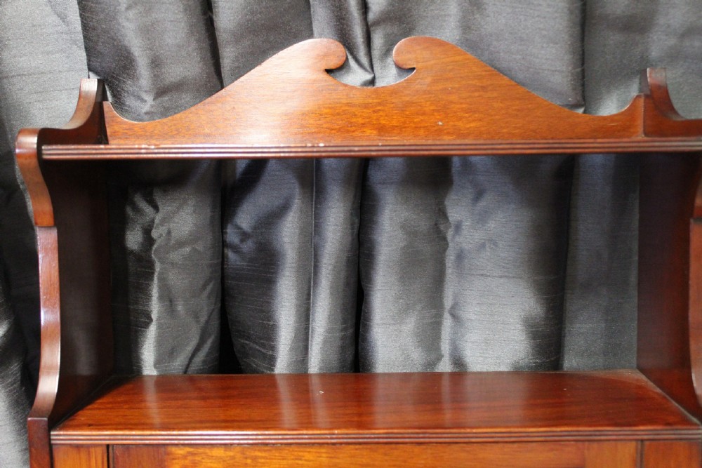 An antique mahogany wall hanging cabinet featuring a central cupboard door with geometric boxwood inlay, a single brass drop handle, a shaped top gallery shelf, and lower side brackets. View III