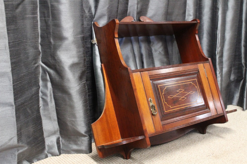 An antique mahogany wall hanging cabinet featuring a central cupboard door with geometric boxwood inlay, a single brass drop handle, a shaped top gallery shelf, and lower side brackets. View IV