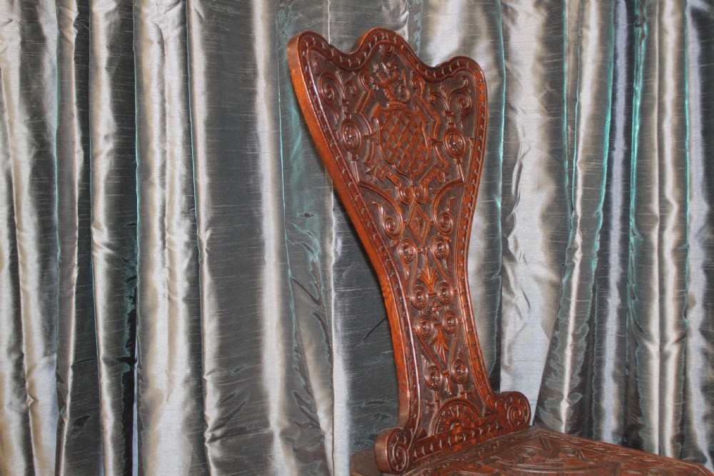 A pair of dark carved oak hall chairs featuring tall shaped backrests with heraldic crest motifs and decorative carved slab bases. View IV
