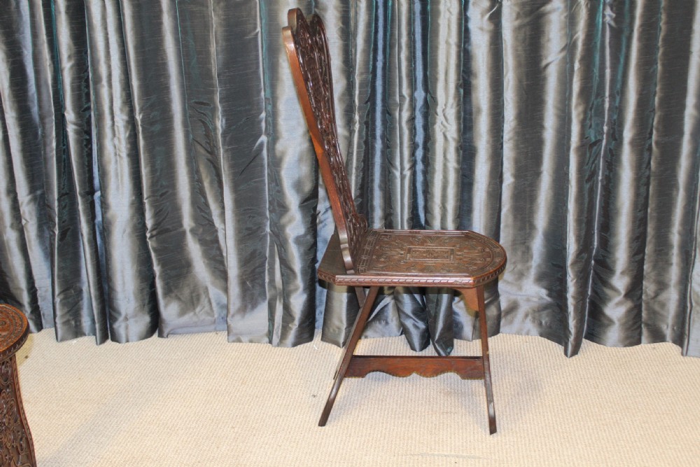 A pair of dark carved oak hall chairs featuring tall shaped backrests with heraldic crest motifs and decorative carved slab bases. View VII