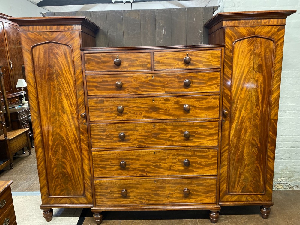 A Victorian flame mahogany compactum wardrobe featuring a central chest of six drawers flanked by twin full-length side cupboards.