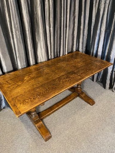 A solid oak refectory dining table featuring a broad rectangular top, twin turned pillar supports, and a floor-level stretcher base.