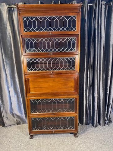 A tall dark mahogany sectional barrister bookcase with five leaded glass door compartments and a central wooden drop-front panel.