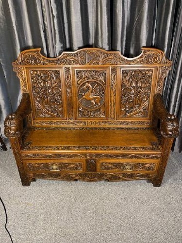 An Edwardian carved oak hall bench dated 1906, featuring mythological beast motifs, foliage panels, carved beast head armrests, and two lower drawers.