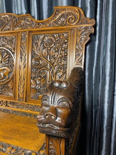 An Edwardian carved oak hall bench dated 1906, featuring mythological beast motifs, foliage panels, carved beast head armrests, and two lower drawers. View II